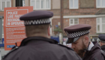 police in front of facial recognition sign